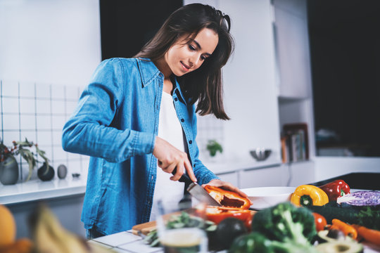 Happy smiling young woman preparing fresh salad in the modern kitchen, smiling hipster girl cooking healthy vegan food with vegetables, organic food lifestyle