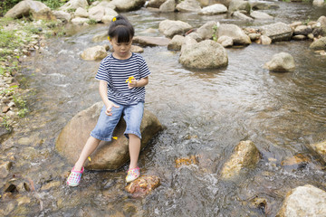 Cute asia little girl is sitting on the rock