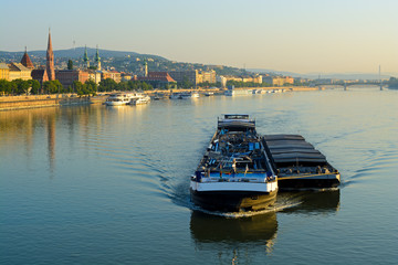 Fototapeta premium cargo ship carrying a barge side by side along still Danube river in Budapest