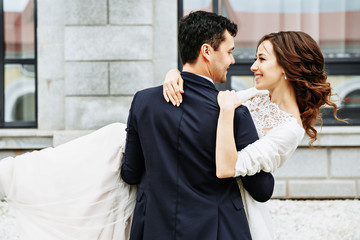 the groom holds his bride in his arms and they dance near the building with beautiful windows