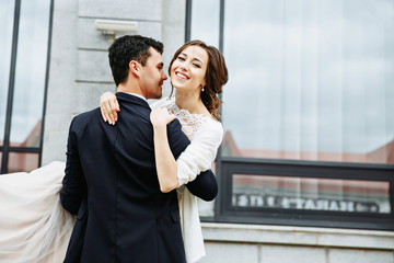 the groom holds his bride in his arms and they dance near the building with beautiful windows