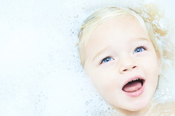 Happy little baby girl face swimming in the bathroomand smile. Portrait of baby bathing in a bath full of foam
