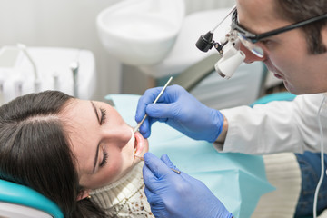 Dentist in magnifying glasses with lighting examines a patient teeth