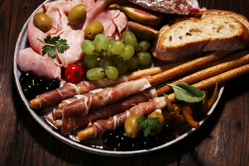 Italian antipasti wine snacks set. Cheese variety, Mediterranean olives, pickles, Prosciutto di Parma, salami and wine in glasses over black grunge background.