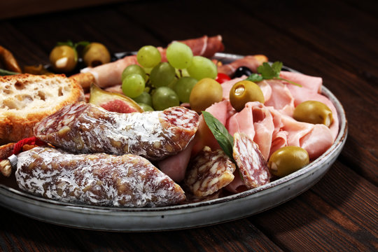 Italian antipasti wine snacks set. Cheese variety, Mediterranean olives, pickles, Prosciutto di Parma, salami and wine in glasses over black grunge background.