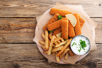 Fish fingers and fries with sauce on wooden table. top view.