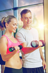 Fototapeta na wymiar fitness, sport, exercising and diet concept - smiling young woman and personal trainer with dumbbells in gym