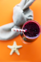 Glass of black currant milkshake or cocktail on orange background. Smoothie from black currant.
