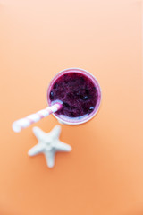 Glass of black currant milkshake or cocktail on orange background. Smoothie from black currant. From top view