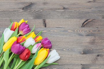 Bouquet of multicolored tulips in a corner on a background of wood.