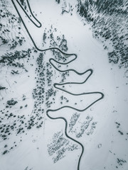 Aerial Photograph of Italian Mountain pass showing a black road winding up the snow covered maountain through pinetrees, Italy 