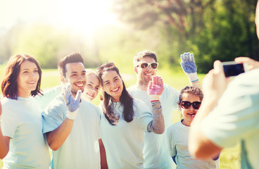 volunteering, charity, people, teamwork and environment concept - group of happy volunteers taking picture by smartphone in park