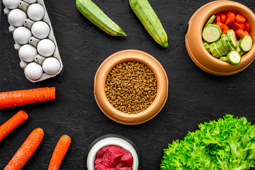 dry organic pet food with fresh vegetables, eggs and meat in plastic bowl for feeding dogs on black background top view mock up