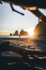 Small person standing on rocky beach in front of giant rock formations with evening glow from the side  near La Push, USA