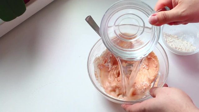 A man is making goulash sauce. Stir the ketchup, sour cream and flour in a glass container with a spoon. Add water and mix again.