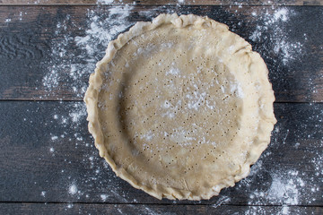 not perfect homemade pie shell with fork marks on dark wood surface sprinkled with white flour flat lay