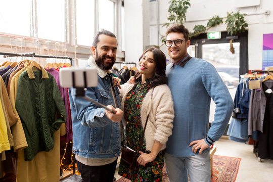 shopping, fashion and people concept - happy smiling friends taking picture by selfie stick at vintage clothing store
