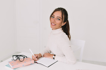 Happy smiling successful  woman works in modern light office with documents. Modern businesswoman. Beautiful young woman looking at camera with smile while sitting  by the table