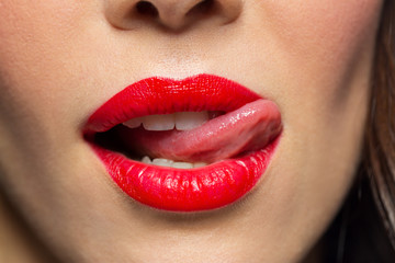 Obraz premium beauty, make up and mouth expression concept - close up of woman face with red lipstick licking her lips