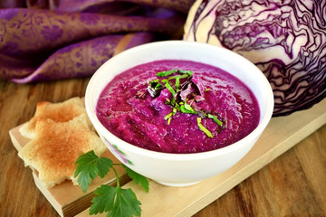 Cream soup made of red cabbage with greenery on wooden table