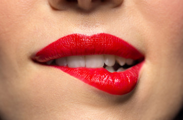 beauty, make up and mouth expression concept - close up of woman face with red lipstick biting...