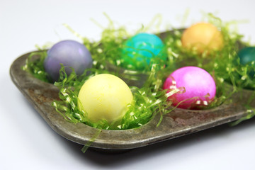 Colorful Easter Eggs sitting on green Easter Grass in Metal Muffin Tin on Bright white Background
