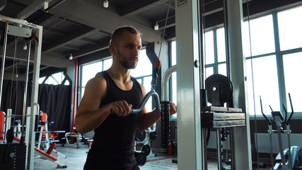 Fototapeta premium Handsome man doing exercise in the simulator with one hand in fitness gym