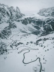 Aerial Photograph of Italian Mountain pass showing a black road winding up the snow covered maountain through pinetrees, Italy 