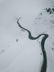 Aerial Photograph of Italian Mountain pass showing a black road winding up the snow covered maountain through pinetrees, Italy 