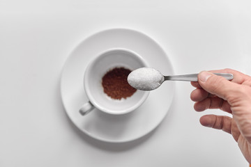Closeup of hand pouring sugar from spoon in cup with coffee