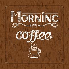 Hand drawn lettering "Morning coffee" with charcoal effect and view of a cup of coffee on brown wood background.