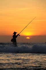 Silhouette of fishermen on the quiet ocean with the rays of sunset at Jimbaran beach, Bali, Indonesia