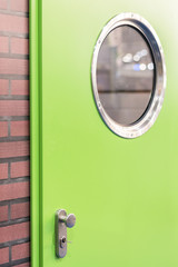 A green door with a round window in a brick wall.