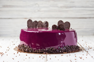 dark chocolate vegan cake with cream and fruit mirror glaze on wooden background