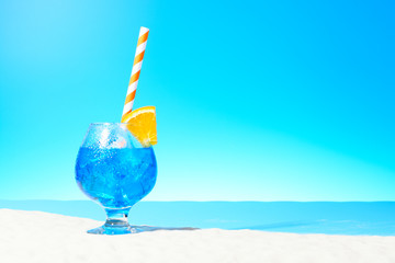 Refreshing blue drink with ice and a slice of orange in a glass on the sandy coast
