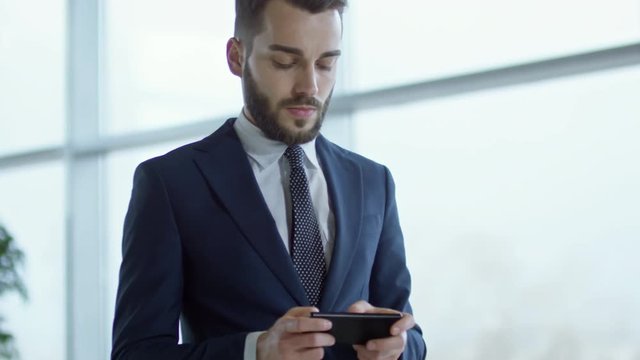 Medium shot of bearded businessman in suit texting on mobile phone