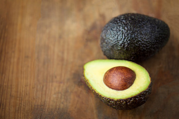 Avocado on a dark wood background. Half and whole avocadoes close up. Top view. Copy space.