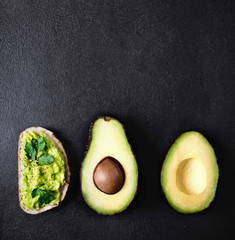 Avocado guacamole on toast bread with spices with Half of avocado on a black background with cop space for text, top view.