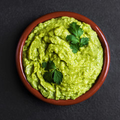 Guacamole spread  in clay bowl on a black background. Avocado sauce. Top view with copy space.
