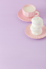 Pastel violet and pink vertical banner with copy space - white zephyr on plate and cup of coffee with milk.