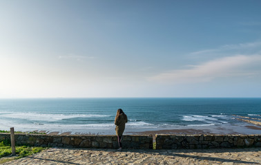 woman seen from the back looking the sea on the horizon.