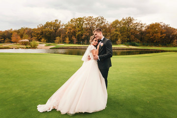 Groom and bride standing on the green grass near the lake at the autumn forest