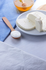 Cheese, honey and sour cream, feta in a white plate, soft cheese on a white background, wooden spoon with sour cream, French breakfast, blue napkin, honey in glassware, art