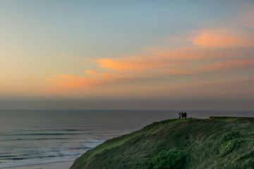 people looking at the horizon from a cliff at sunset