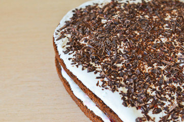 Close up of a homemade cake covered with chocolate and cream on wooden background.