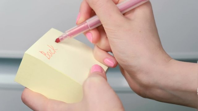 Closeup woman's hands write on yellow sticker paper sheets words back at 12:00.