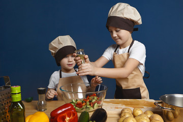 Candid shot of cute little boy wearing chef hat standing at kitchen table and watching his serious...
