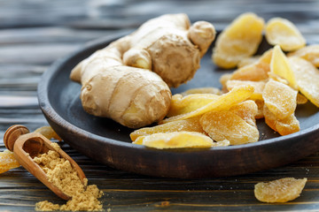 Ginger root and candied ginger on a wooden plate.