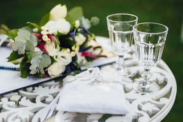 Wedding rings with glasses and bouquet on the ceremony table.