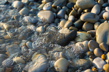 pebble stones on the sea beach, the rolling waves of the sea with foam